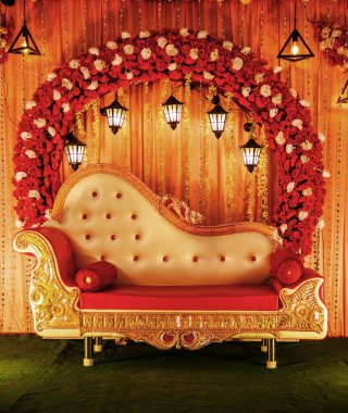 Büyüleyici bir düğün sahnesi tasarımı, canlı çiçekler, güzel süslü bir kanepe, ve sıcak ışıklandırma, özel günler ve kutlamalar için mükemmel bir atmosfer hazırlıyor..