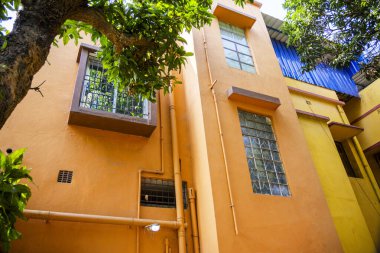 Renkli bina cephesinde parlak turuncu ve sarı tonlarda, geniş pencereli, yemyeşil yeşilliklerle çevrili, kentsel çevrenin canlı ve canlı görünümünü yakalıyor..