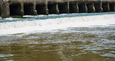 Bereketli yeşilliklerle çevrili, beton bir yapının üzerinden akan sakin ve istikrarlı su, doğanın mühendislik yapılarıyla olan etkileşiminin güzelliğini gözler önüne seriyor, çevresel veya endüstriyel kavramlar için mükemmel..