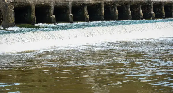 Bereketli yeşilliklerle çevrili, beton bir yapının üzerinden akan sakin ve istikrarlı su, doğanın mühendislik yapılarıyla olan etkileşiminin güzelliğini gözler önüne seriyor, çevresel veya endüstriyel kavramlar için mükemmel..