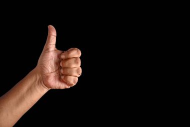 Sağlam bir siyah arkaplana karşı, olumlu, onay ve başarıyı sembolize eden baş parmak hareketi yapan bir elin yakın çekimi. Münferit ortamda teşvik ve anlaşma mesajı vurgulanıyor.