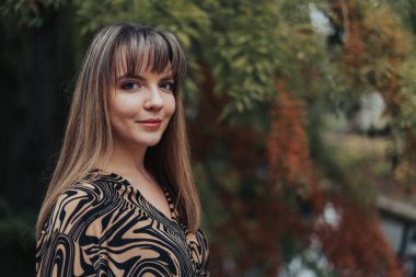 Elinde yapraklar olan bir kadın, parkta duruyor.