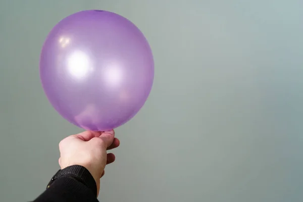 Young Man Holding a Purple Balloon in hand in front of a Grey Background