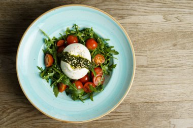 Arugula, Pesto ve domates soslu Burrata Caprese Peynir Salatası, ahşap bir masada. Yüksek Açı Görünümü