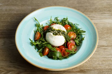 Arugula, Pesto ve domatesli Burrata Caprese Salatası ahşap bir masada.