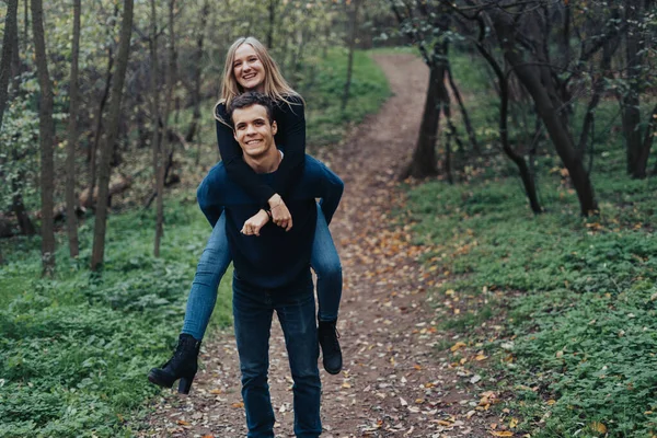 森の中でピギーバックしながら楽しい時間を過ごしている若い陽気なカップル — ストック写真