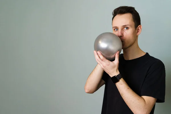 Young Man Blowing a Balloon Against Grey Background