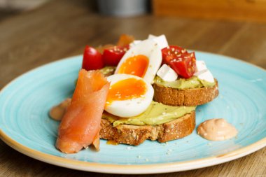 Avokado tostlu guacamole, haşlanmış yumurta, somon, krem peynir ve domatesli bir tabak..