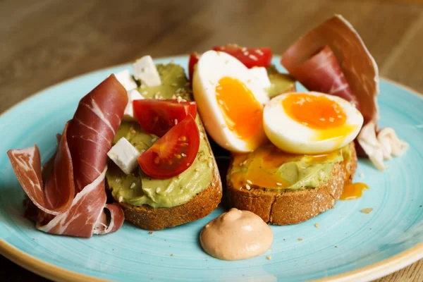 Avokado tostu ile guacamole, rafadan yumurta, jambon, krem peynir ve domates tabakta..