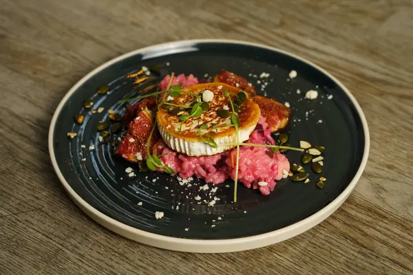 Pancarlı risotto, ızgara keçi peyniri, incir ve ahşap masada kızartılmış kabak çekirdeği.