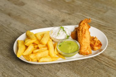 Tahta masadaki tartar soslu balık ve patates kızartması.