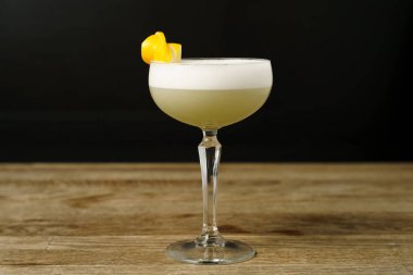 Ahşap bir masada limon kabuğu ve buz dilimli bir kokteyl.