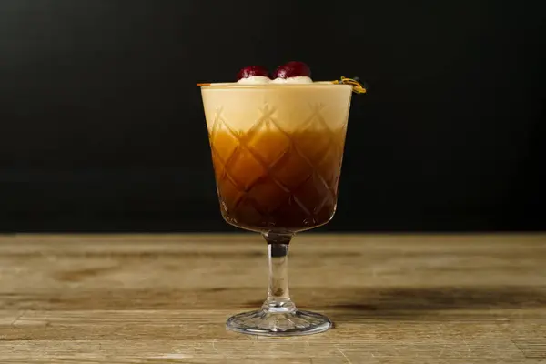 A cocktail with cherry, coffee and ice on a wooden table