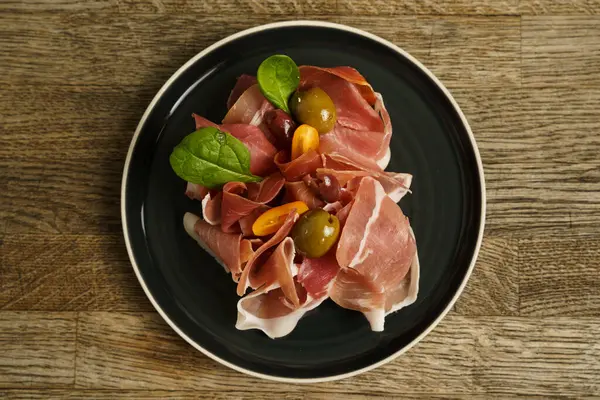 Prosciutto ham plate with olives on wooden table