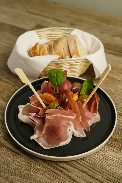 Prosciutto ham plate with olives and bread on wooden table
