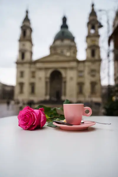 A pink rose and a coffee cup on a table in front of basilica