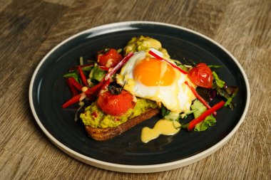 Tahta bir masada kızarmış yumurta ve sebzeli avokado tostu.