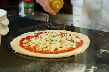 Bir şef domates soslu ve mozzarella peynirli pizza hazırlıyor, pizzaya zeytinyağı sürüyor.