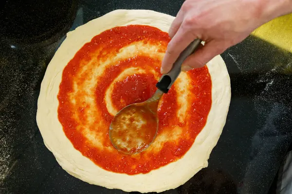 stock image Top down view of spreading tomato sauce on pizza dough with a spoon