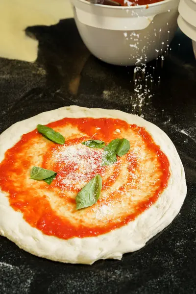 stock image A chef preparing a pizza with tomato sauce and spreading parmesan cheese