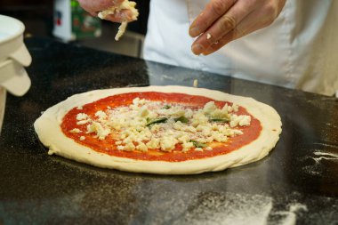 Bir şef domates soslu pizza hazırlıyor ve pizzaya mozzarella peyniri sürüyor.