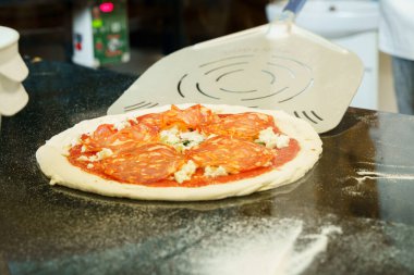 Aşçı pizza hamurunu fırına koymadan önce kürekle hazırlıyor ve yayıyor.