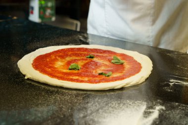 Bir şef domates soslu pizza hazırlıyor.