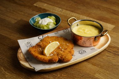 Lezzetli bir porsiyon limon dilimli altın esmer şnitzel, yanında bakır bir tencerede kremalı patates püresi ve ekşi kremalı salata.. 