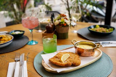 Lezzetli bir porsiyon limon dilimli altın esmer şnitzel, yanında bakır bir tencerede kremalı patates püresi ve ekşi kremalı salata..