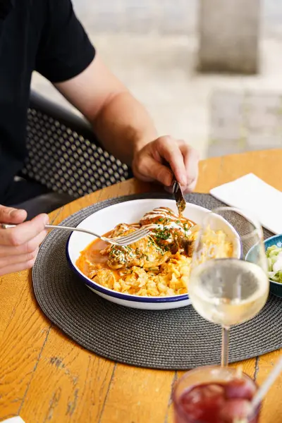 Üzeri ekşi krema ve soğanlı Paprika tavuğu, yanında kremalı spaetzle ve ekşi kremalı salatayla servis edilir. Elleri tabağı keserken görülüyor..