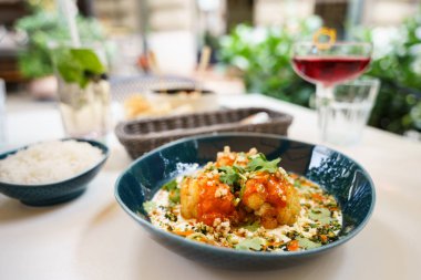 Baharatlı sosla kaplanmış, taze otlarla süslenmiş ve mavi bir kasede servis edilen kavrulmuş karnabahar içeren bir yemek. Lezzetli yemeğe bir kase pilav eşlik eder..