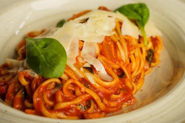 Taze fesleğen yaprakları ve tıraş edilmiş parmesan peyniri ile süslenmiş domates soslu güzel bir tabak spagetti. Yemek kırsal bir seramik kasede sunuluyor, sıcak ve davetkar bir sunum yaratıyor..