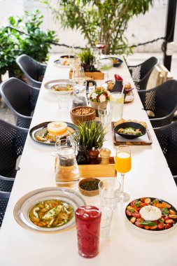 Salatalar, çorbalar, taze meyve suları ve aperatifler de dahil olmak üzere çeşitli yemek ve içeceklerle dolu güzel bir açık hava brunch masası. Bu ortam sosyal bir yemek için idealdir..