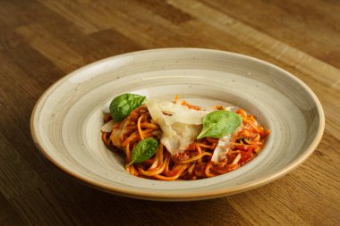 Taze fesleğen yaprakları ve tıraş edilmiş parmesan peyniri ile süslenmiş domates soslu güzel bir tabak spagetti. Yemek kırsal bir seramik kasede sunuluyor, sıcak ve davetkar bir sunum yaratıyor..