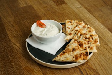 Bir porsiyon ızgara pita ekmeği ve bir kase kremalı tzatziki sosu, vişneli domatesle süslenmiş. Bu yemek Akdeniz 'den esinlenilmiş bir aperatif ya da aperatifi somutlaştırır..