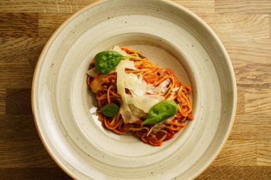 Taze fesleğen yaprakları ve tıraş edilmiş parmesan peyniri ile süslenmiş domates soslu güzel bir tabak spagetti. Yemek kırsal bir seramik kasede sunuluyor, sıcak ve davetkar bir sunum yaratıyor..