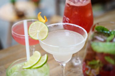 Her birinde limon dilimleri, portakal kabukları ve nane gibi eşsiz garnitürler bulunan canlı bir kokteyl çeşidi. İçecekler arasında tuz kenarlı bir margarita, pembe bir kokteyl ve ferahlatıcı yeşil bir içecek var.