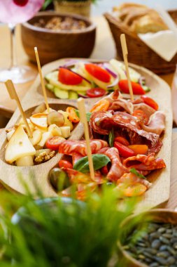 Pişmiş et, peynir, domates ve salatalıklı taze salata ve bir sepet dilimlenmiş ekmek içeren kırsal bir şarküteri tahtası. Yayılım, hafif bir aperatif ya da aperatif olarak paylaşmak için ideal doku ve tatlar sunuyor..