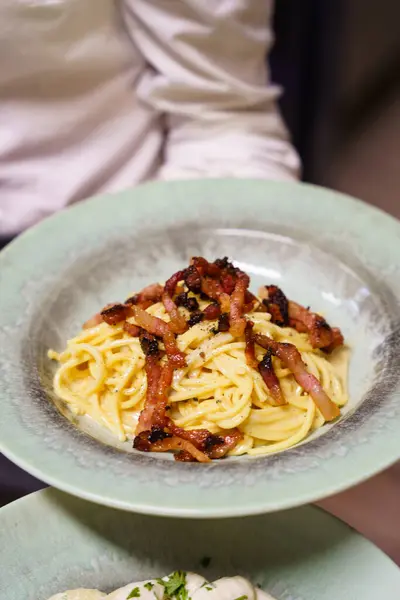 Çıtır pancetta ve taze karabiberle kaplı bir tabak spagetti. Kremalı sos ve altın makarna bu klasik yemeğin otantik İtalyan lezzetini vurgular..