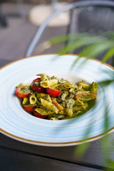 Çilekli domates ve doğranmış etle süslenmiş taze pesto sosuyla kaplı lezzetli bir makarna tabağı. Tabak mavi çizgili bir seramik kasede servis ediliyor..
