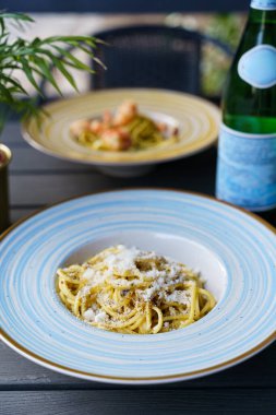Pecorino Romano peyniri ve taze siyah biberle kaplanmış al dente spagetti içeren bir tabak otantik İtalyan kakio e pepe pasta. Tabak mavi çizgili bir seramik kasede servis edilir..