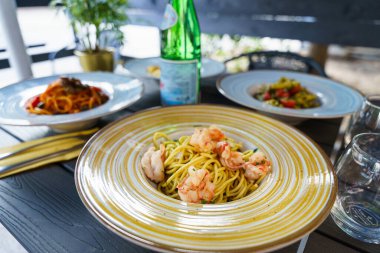 Renkli İtalyan makarna tabakları ve bir şişe köpüklü su ile açık hava masası taze ve davetkar bir Akdeniz yemek atmosferi yaratıyor..