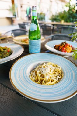 Renkli İtalyan makarna tabakları ve bir şişe köpüklü su ile açık hava masası taze ve davetkar bir Akdeniz yemek atmosferi yaratıyor..