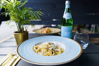 Pecorino Romano peyniri ve taze siyah biberle kaplanmış al dente spagetti içeren bir tabak otantik İtalyan kakio e pepe pasta. Tabak mavi çizgili bir seramik kasede servis edilir..