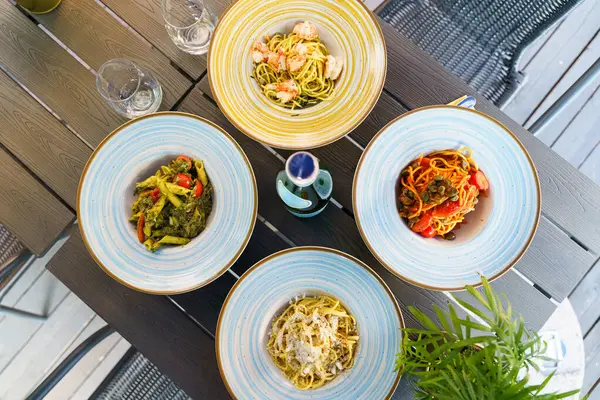 Renkli İtalyan makarna tabakları ve bir şişe köpüklü su ile açık hava masası taze ve davetkar bir Akdeniz yemek atmosferi yaratıyor..