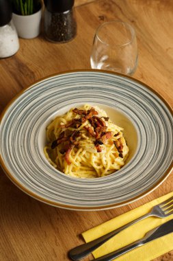 Çizgili seramik tabakta gevrek pancetta ile kaplanmış güzel kaplanmış bir spagetti carbonara. Kremalı sos ve altın renkler sıcak ve kırsal bir İtalyan yemeği deneyimi yaratır..