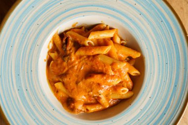 Zengin, kremalı domates sosuyla kaplanmış, mavi ve beyaz çerçeveli bir tabakta servis edilen lezzetli bir makarna tabağı. Canlı turuncu rengi rahatlatıcı ve doyurucu bir yemek olduğunu gösteriyor..