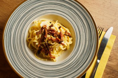 Çizgili seramik tabakta gevrek pancetta ile kaplanmış güzel kaplanmış bir spagetti carbonara. Kremalı sos ve altın renkler sıcak ve kırsal bir İtalyan yemeği deneyimi yaratır..