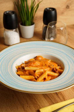 Zengin, kremalı domates sosuyla kaplanmış, mavi ve beyaz çerçeveli bir tabakta servis edilen lezzetli bir makarna tabağı. Canlı turuncu rengi rahatlatıcı ve doyurucu bir yemek olduğunu gösteriyor..