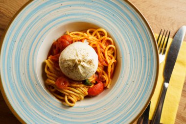 Bir burrata topuyla kaplı bir spagetti tabağı, kiraz domatesli ve fesleğenli domates sosuyla servis ediliyor. Kremalı peynir, canlı makarnayla çok güzel zıtlaşıyor..